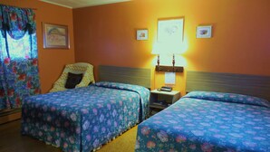 A hotel room with two beds, a nightstand with a lamp, and a window with floral curtains. - Four Seasons Motel (Catskill)