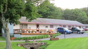 A motel with a porch, a small stream, and parked vehicles. - Four Seasons Motel (Catskill)