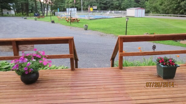 A wooden deck with a flower pot and a view of a playground area with picnic tables and a small shed. - Four Seasons Motel (Catskill)