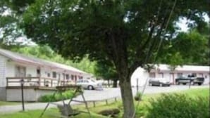 A motel with a single-story structure, a covered parking area, and a swing set in the yard. - Four Seasons Motel (Catskill)