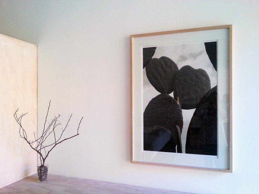 A framed abstract painting on a wall, a vase with a branch on a table, and a plain wall.