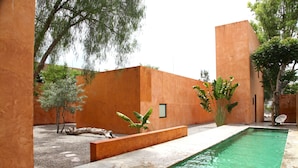 Una piscina con plataforma de hormigón, rodeada de muros anaranjados y árboles.