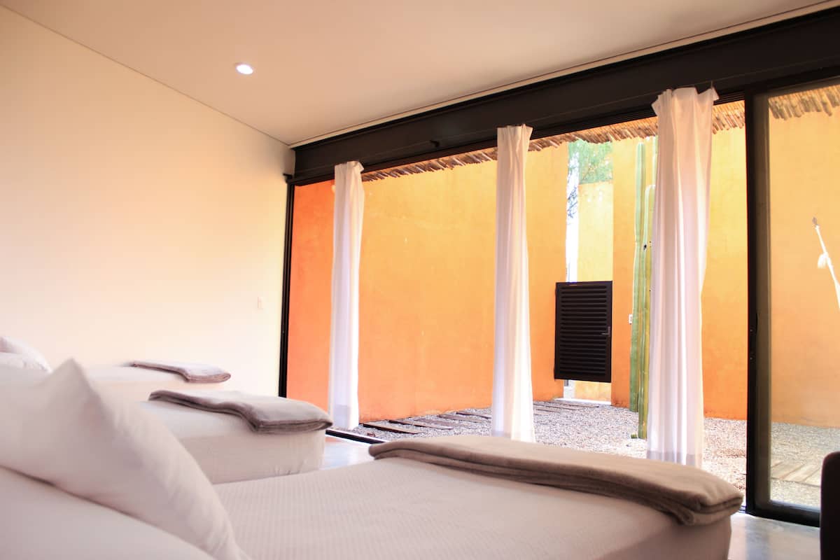 Habitación de hotel con cama, almohadas y vista a un área exterior con techo de paja y un cactus.