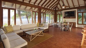 Ein großzügiger Wohnbereich mit einer großen Couch, einem Esstisch und Stühlen mit Blick auf einen Strand.