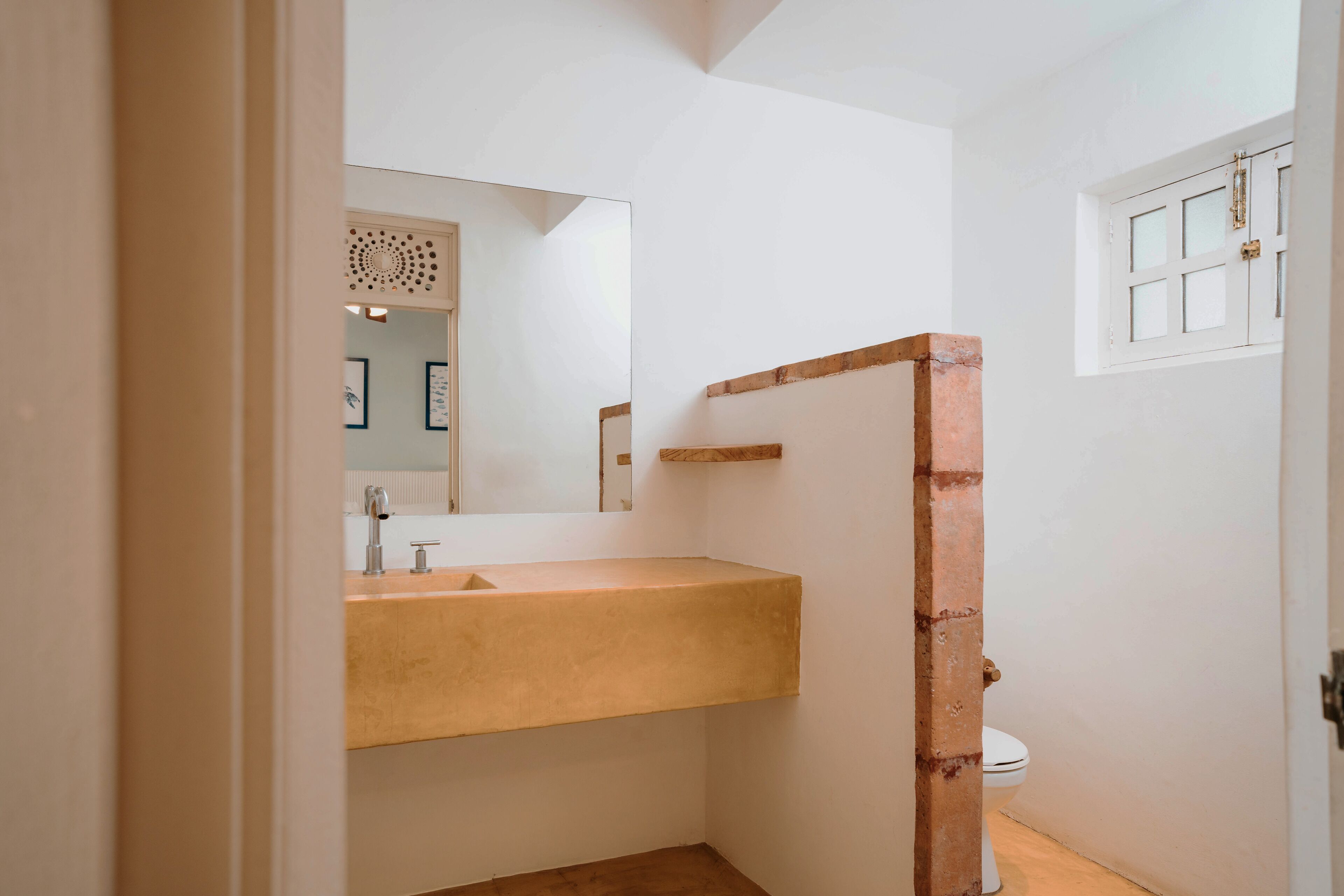 Une salle de bain avec un meuble-lavabo en bois, des toilettes et une fenêtre donnant sur l’extérieur.