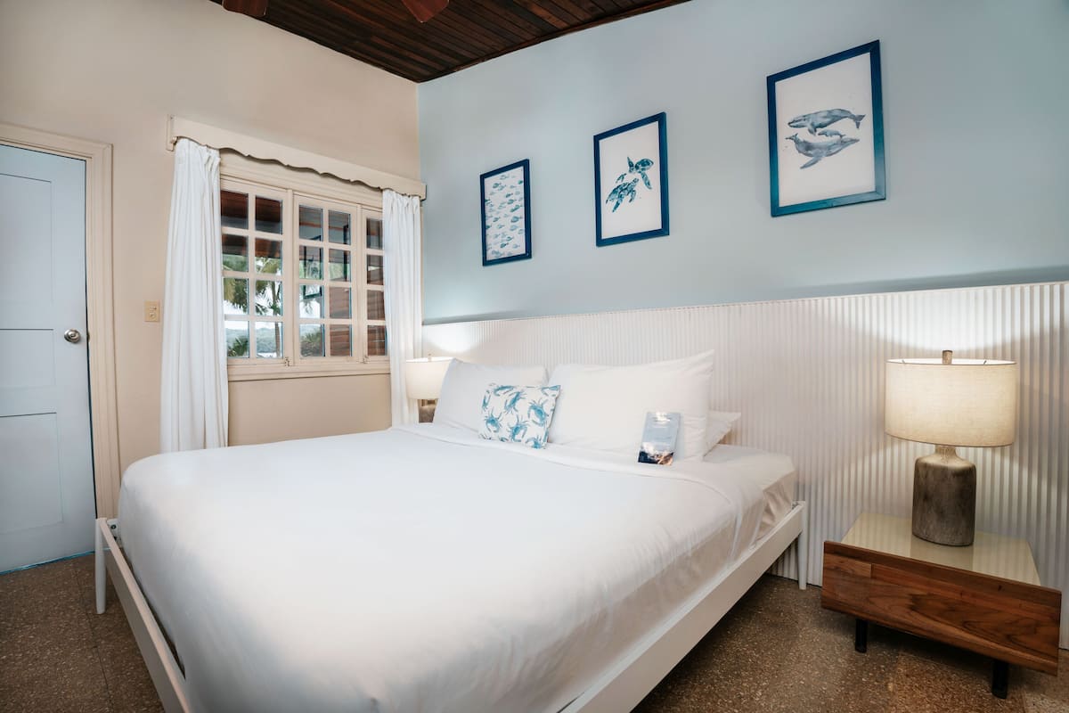 Een slaapkamer met een bed, een nachtkastje, een raam met gordijnen en drie ingekaderde foto's aan de muur.