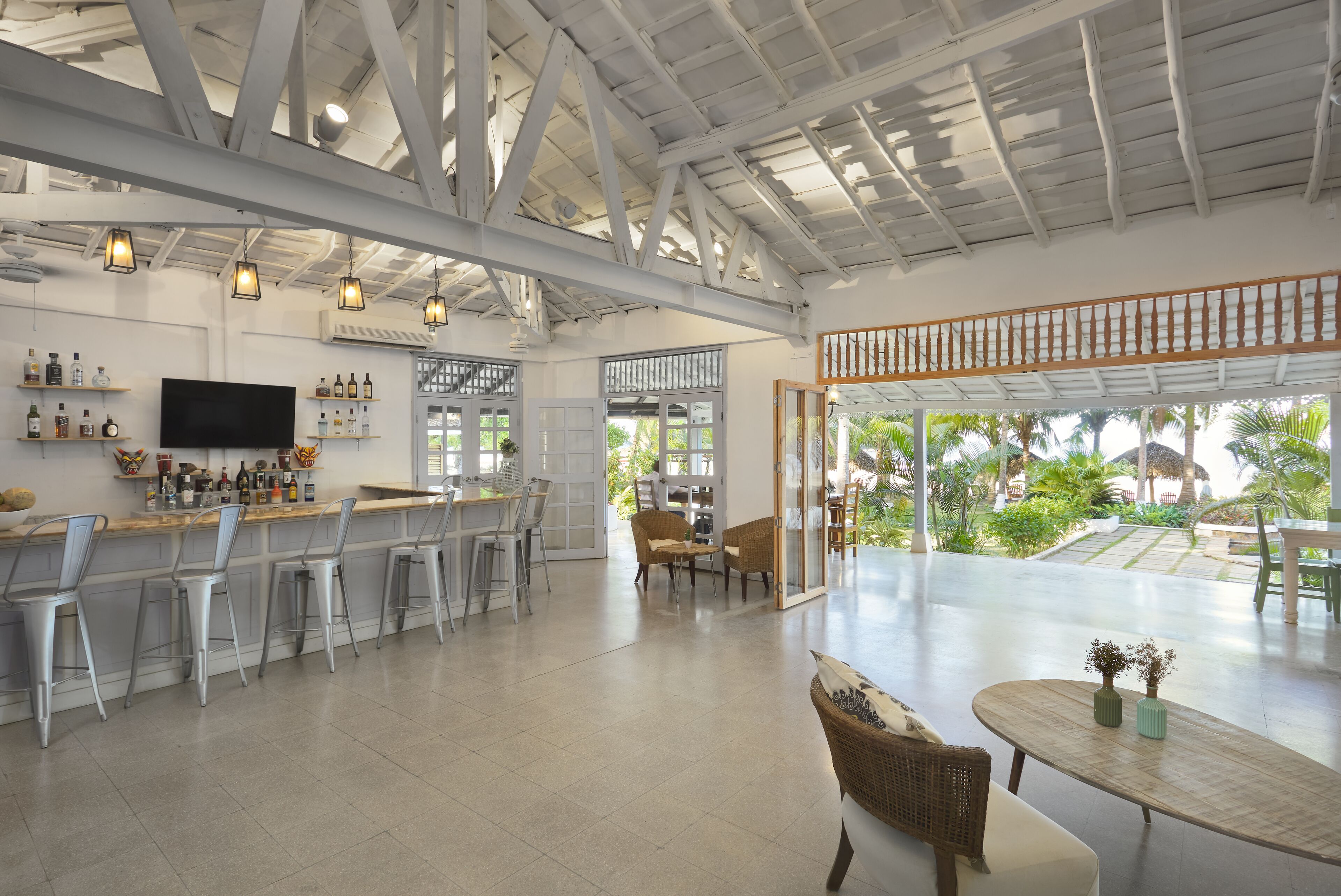 A spacious bar area with high ceilings and natural light, a television, and a view of the outdoor garden.