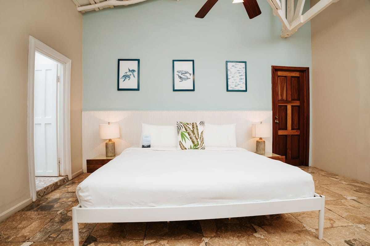 Een slaapkamer met een wit bed, een houten deur en wanddecoratie in lijsten.
