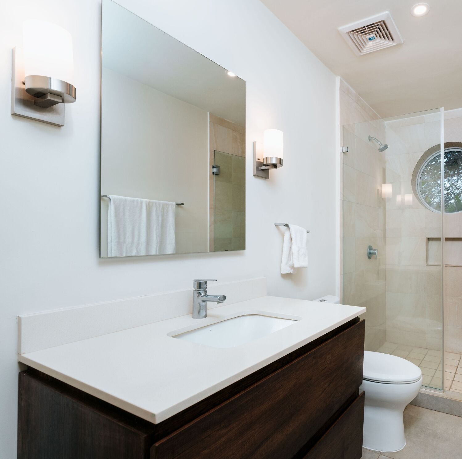 Een moderne badkamer met een grote spiegel, een witte wastafel en een douche met glazen wanden.
