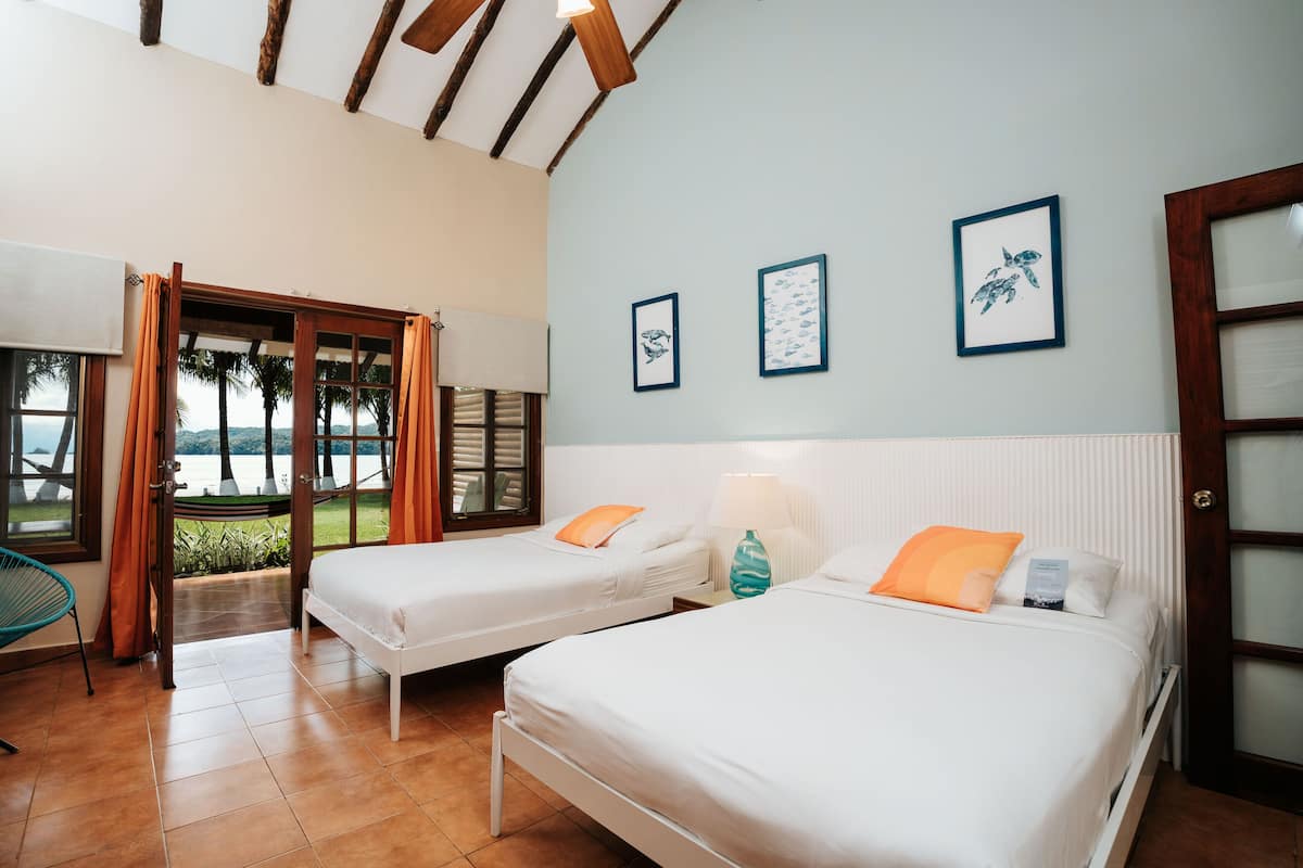 Een hotelkamer met twee bedden, uitzicht op de omgeving en drie ingelijste foto’s aan de muur.