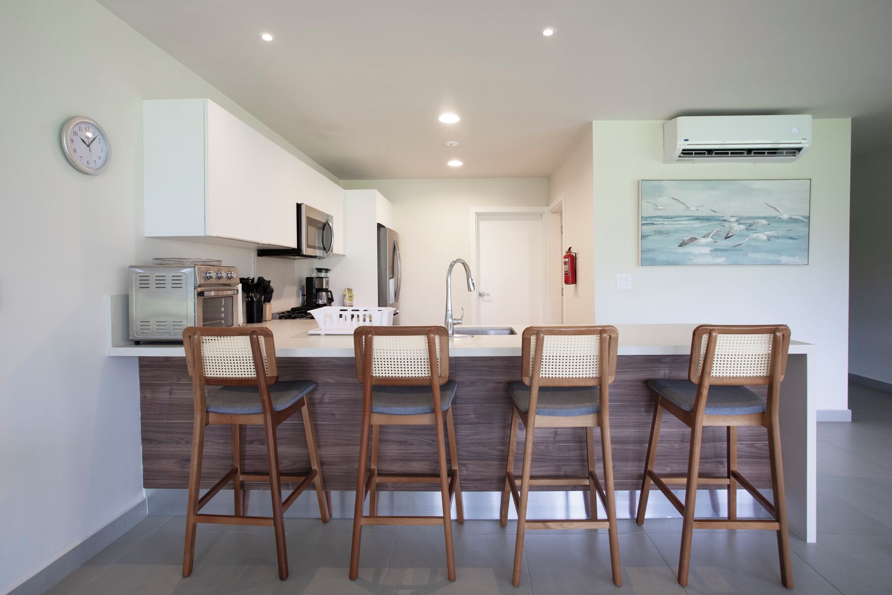 Una cocina moderna con una isla central, cuatro sillas de madera, un reloj y un cuadro en la pared.
