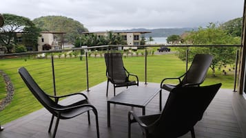 Un balcón con tres sillas y una mesa, con vistas a un césped cuidado y una masa de agua.