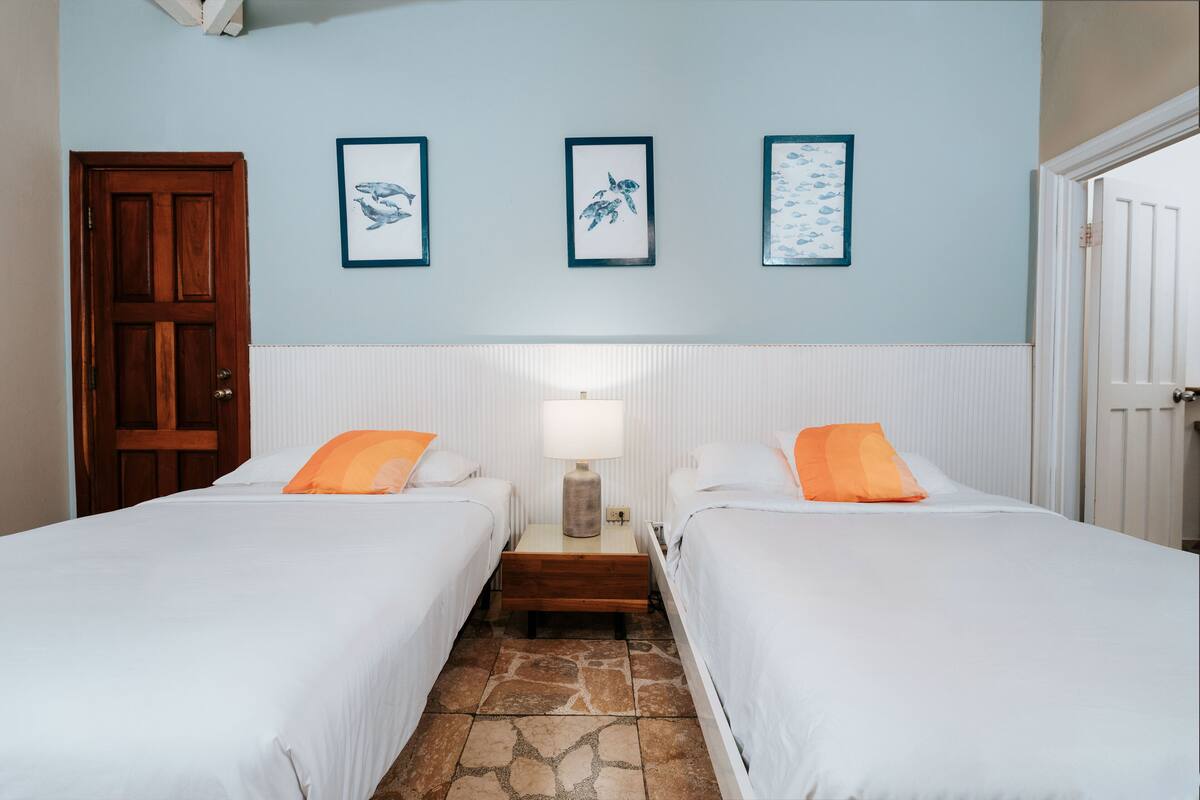 Een hotelkamer met twee bedden, een nachtkastje met een lamp en drie ingelijste foto’s aan de muur.