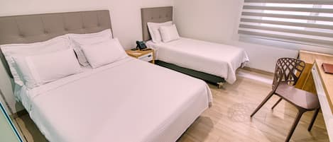 A hotel room with two beds, a desk, a chair, and a window with blinds.