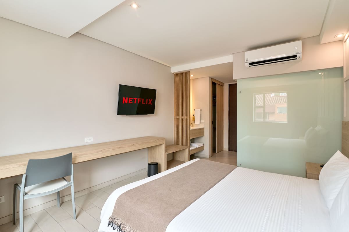 Une chambre d’hôtel moderne équipée d’un lit, d’un bureau, d’une chaise, d’un téléviseur fixé au mur et d’un appareil de climatisation.