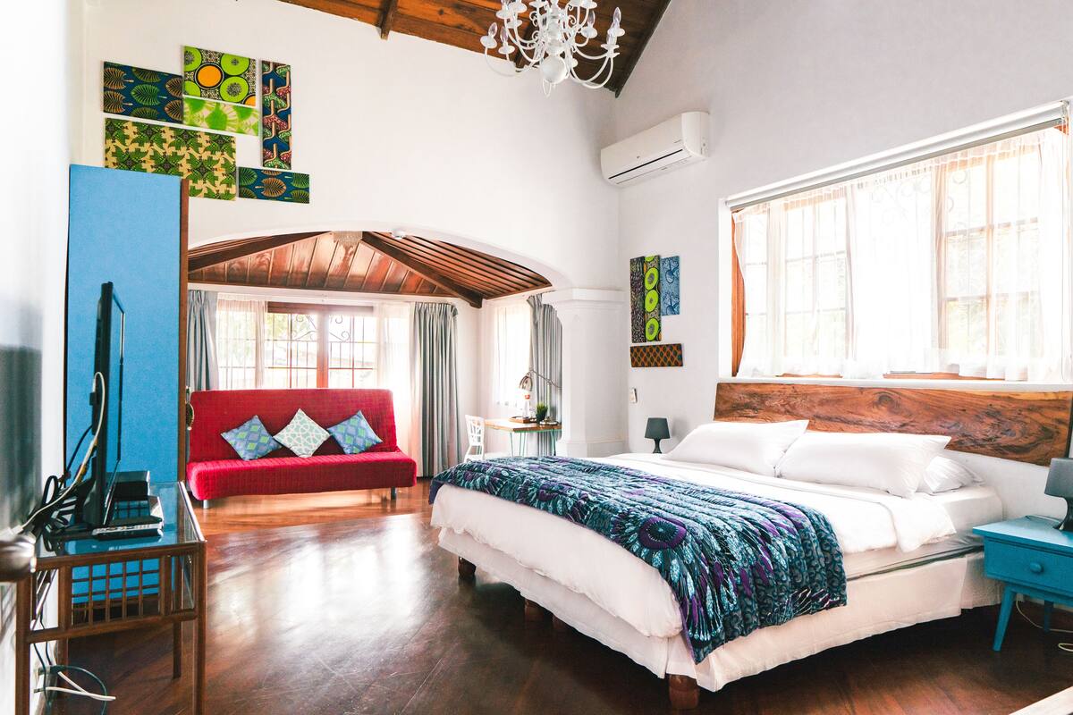 Un dormitorio con una cama grande, un sofá rojo, techo de madera y una lámpara de araña.