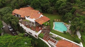 Una casa grande con piscina, rodeada de abundante vegetación y un jardín cuidado.