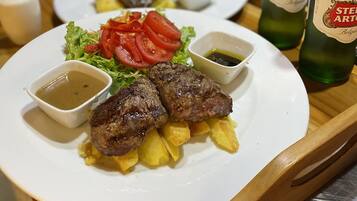 Una bandeja con platos de comida que incluyen carne, patatas y verduras, y dos botellas de cerveza Stella Artois.