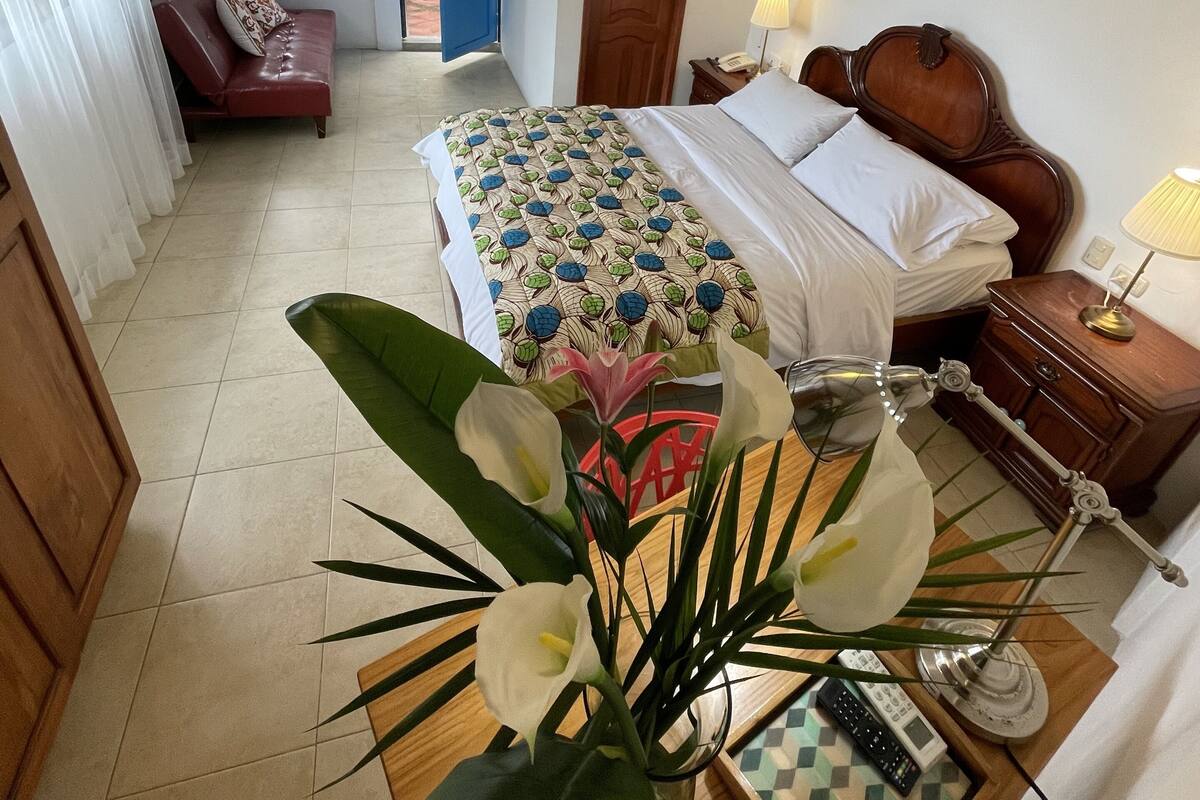 Un dormitorio con cama, mesita de noche, lámpara y un jarrón con flores.