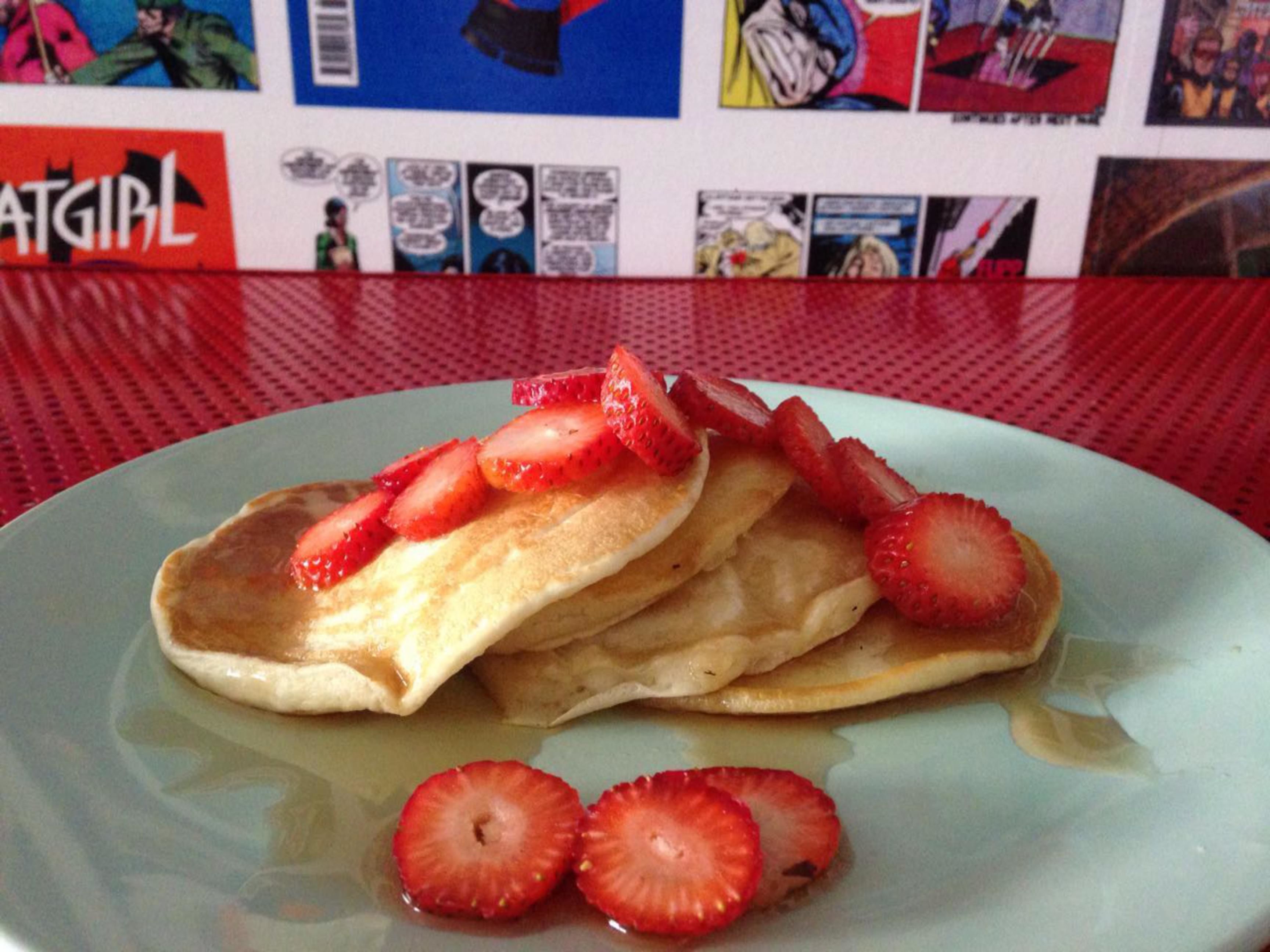 Una torre de panqueques con fresas sobre una mesa con mantel rojo.