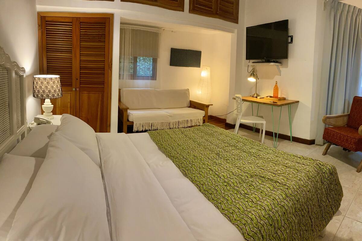 Habitación de hotel con cama, escritorio, silla, televisor y ventana con cortinas.
