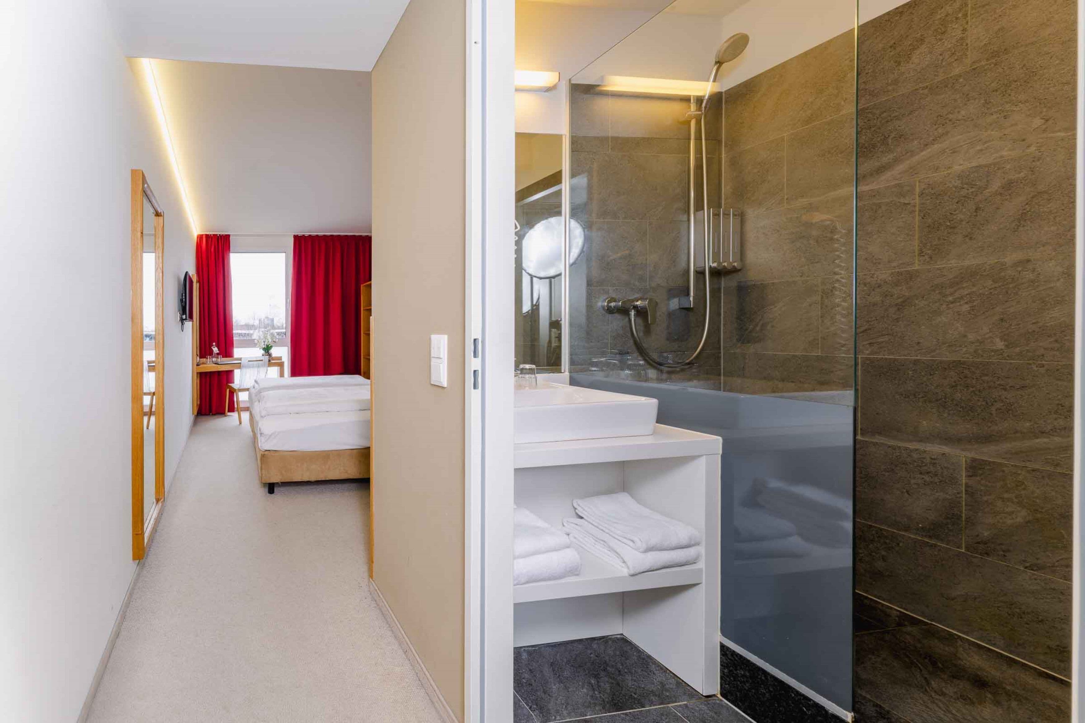 Habitación de hotel con cama, baño con cabina de ducha de vidrio y una pequeña zona de estar con mesa y sillas.