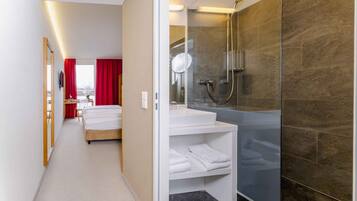 Habitación de hotel con cama, baño con cabina de ducha de vidrio y una pequeña zona de estar con mesa y sillas.