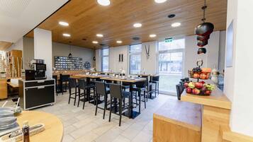 Un café moderno con techo de madera, mesas redondas, sillas negras y una exhibición de frutas.