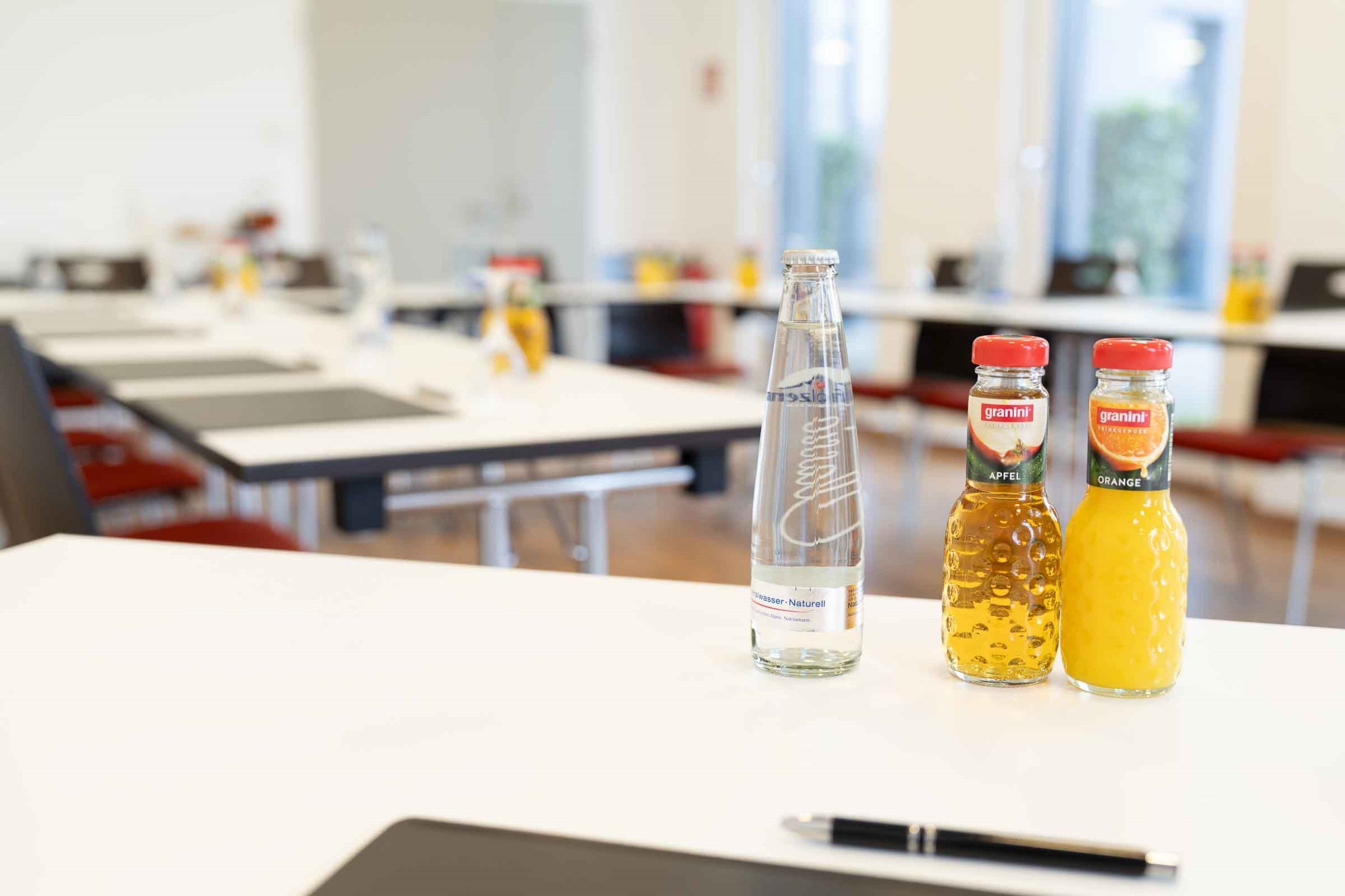 Un aula con mesas y sillas, una botella de agua y dos botellas de zumo de naranja Granini.