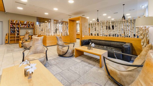 A modern lounge area with leather sofas, a wooden coffee table, and a bookshelf. - PLAZA INN Dachau - München (Dachau)