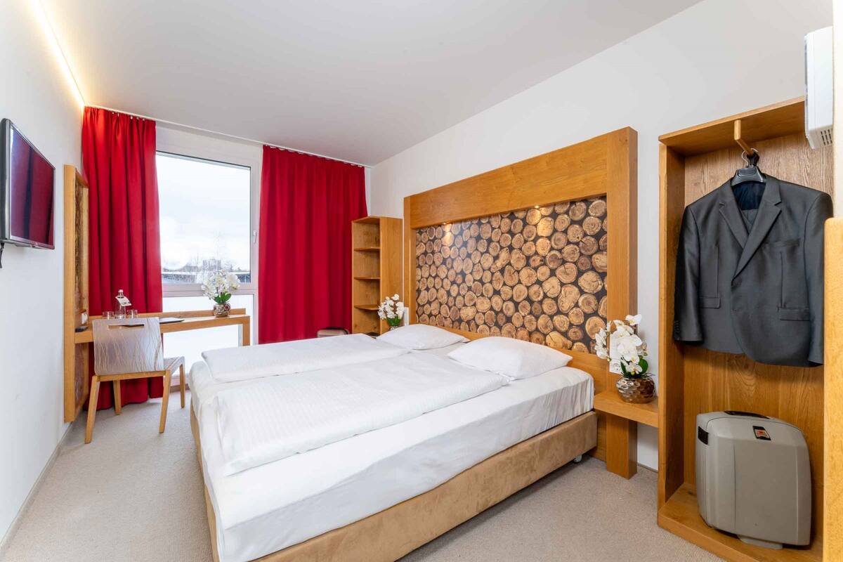 A hotel room with a bed, a desk, a TV, a coat rack, and a wall with a log pattern.