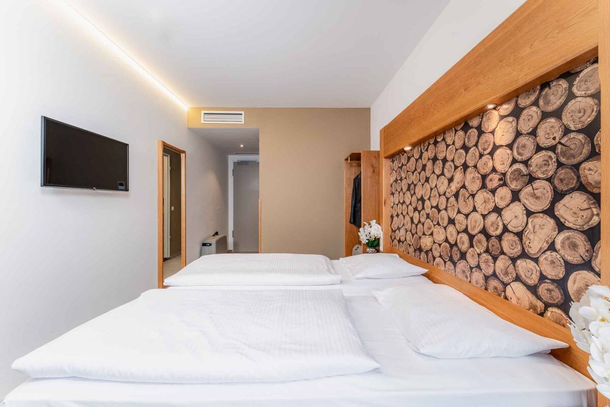 A hotel room with two beds, a flat-screen TV mounted on the wall, and a wooden log wall.