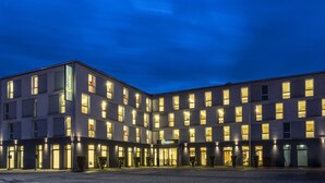 A modern hotel with multiple floors, illuminated windows, and a prominent entrance. - PLAZA INN Dachau - München (Dachau)