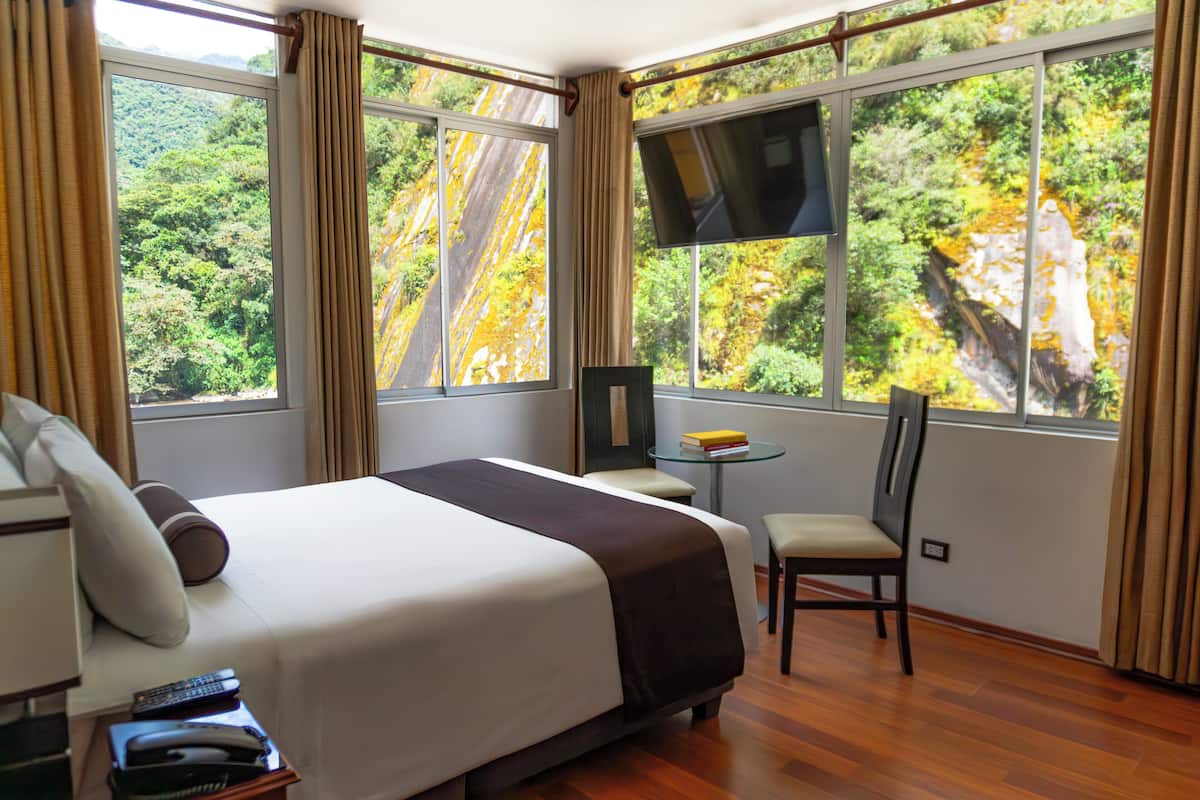 A hotel room with a large bed, a TV, a small table with books, and a chair.