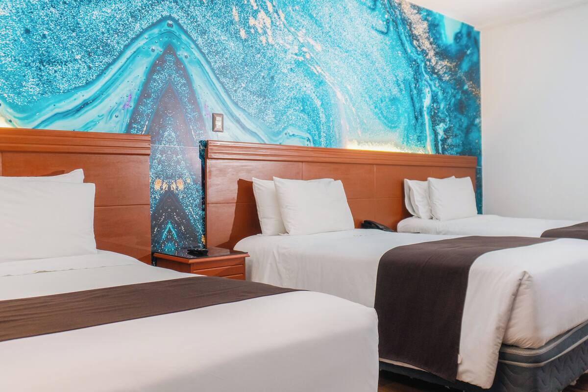 A hotel room with three beds, a wooden headboard, and a large abstract painting on the wall.