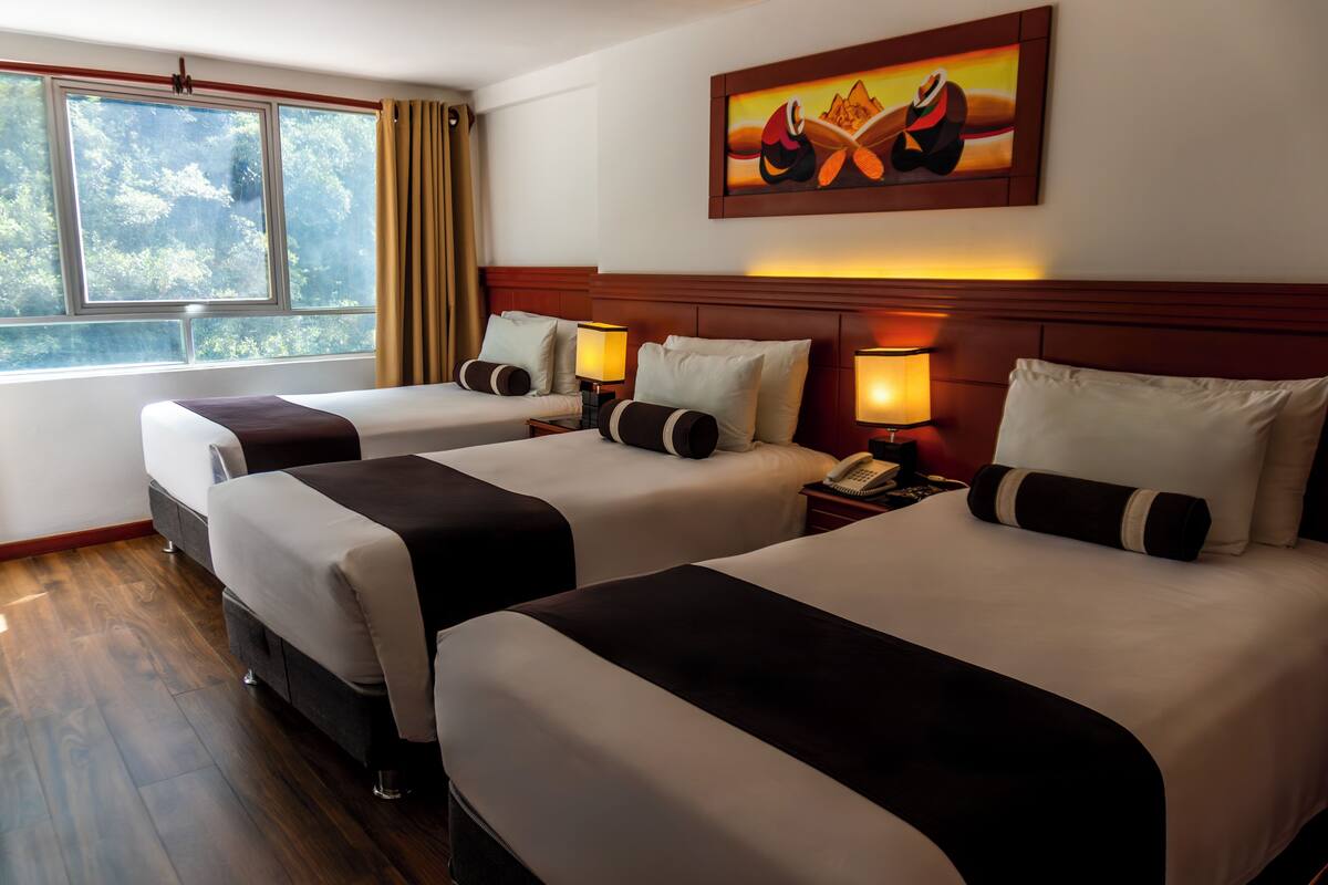 A hotel room with two beds, a painting on the wall, and a window with curtains.