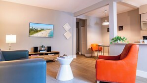 A modern living room with a blue sofa, an orange armchair, a white coffee table, and a painting of a beach scene on the wall. - Beachside All Suites Hotel (Miami Beach)