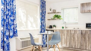 A modern kitchen with a dining area, featuring a round table, two chairs, and a built-in stove. - Beachside All Suites Hotel (Miami Beach)
