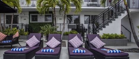 A hotel with outdoor lounge chairs, a staircase, and palm trees.