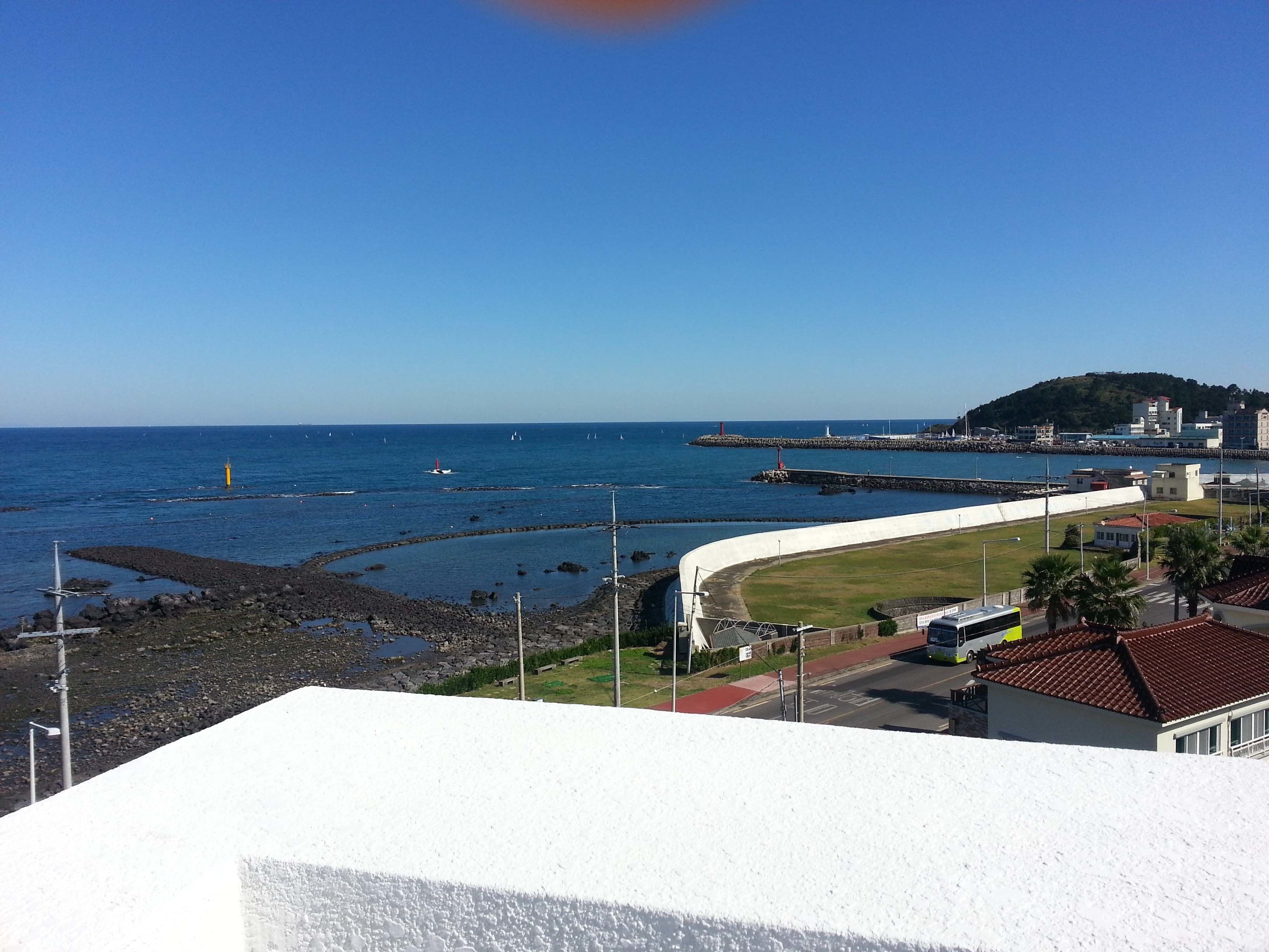 Vista costera con un edificio blanco, una carretera serpenteante y un muelle distante.