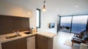 A modern kitchen with a built-in dishwasher, a large window overlooking the sea, and a cozy seating area with a sofa and a table. - Vista View Resort (Jeju City)