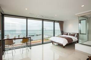 Ein modernes Schlafzimmer mit großem Fenster und Meerblick, einem Bett, einem Schreibtisch mit Stuhl sowie einer Glastrennwand.