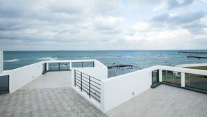 A modern building with a terrace overlooking the sea, featuring a white exterior and glass railings. - Vista View Resort (Jeju City)