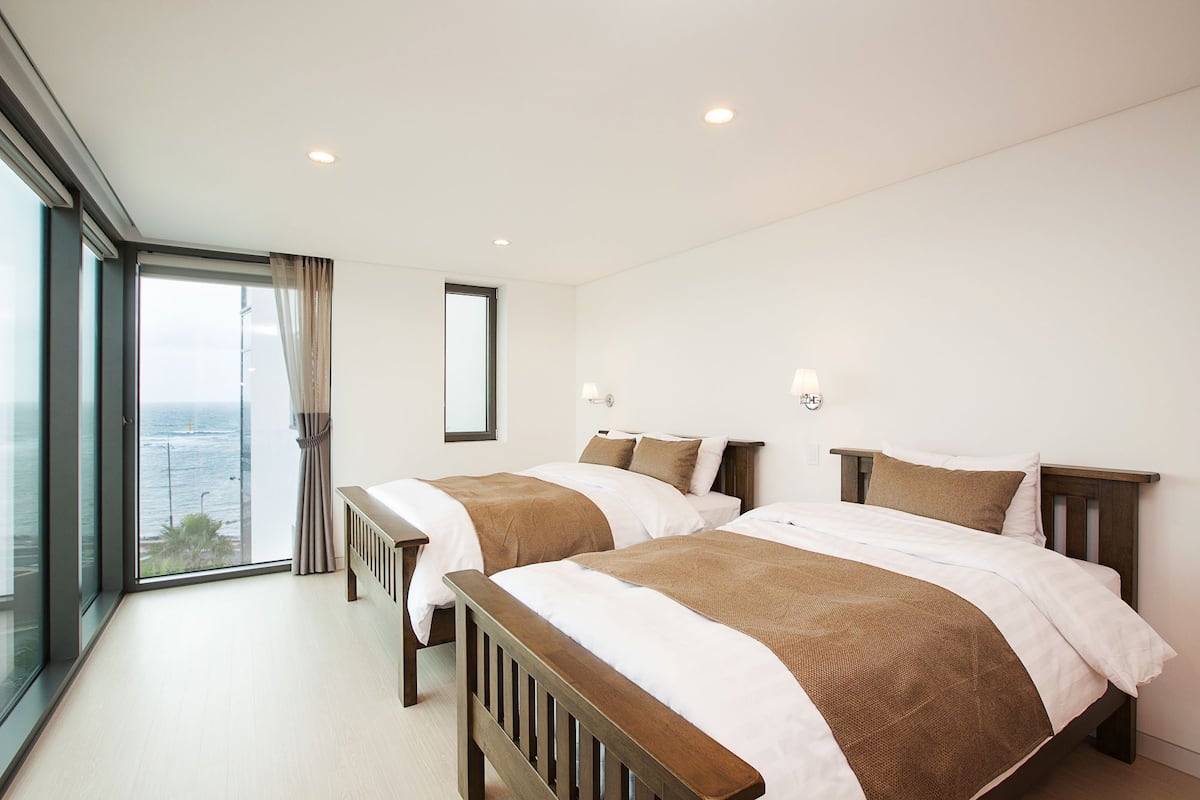 Habitación de hotel con dos camas, ventanas amplias y vista al mar.