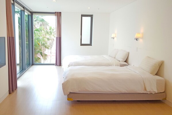 Ein Hotelzimmer mit einer großen Glasschiebetür, die auf einen Balkon führt, einem Bett mit weißer Bettwäsche und zwei Wandleuchten.