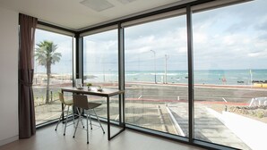 A modern room with large windows overlooking a beach and road. - Vista View Resort (Jeju City)