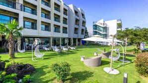 A hotel courtyard with outdoor seating, a palm tree, and a modern building with balconies. - Pension Yeoli (Seogwipo)