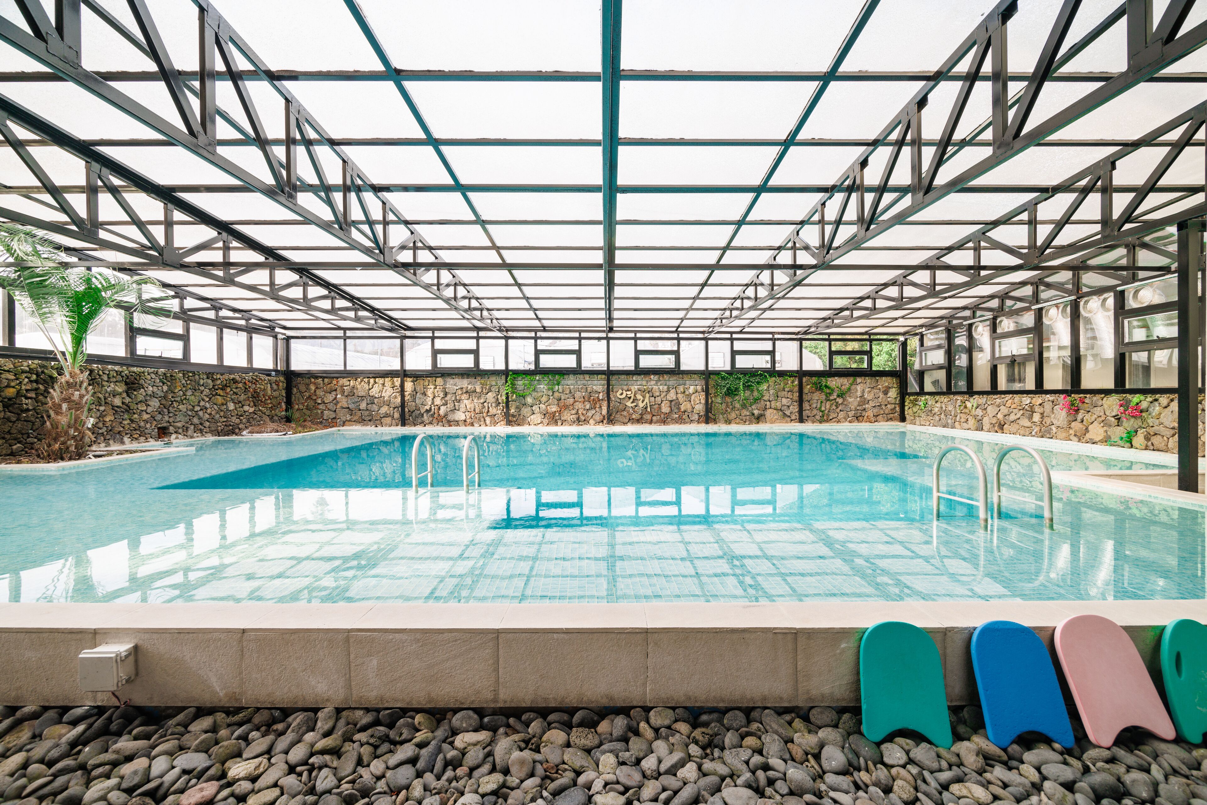 An indoor swimming pool with a stone wall and metal framework.