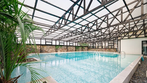 An indoor swimming pool with a glass ceiling, surrounded by rocks and palm plants. - Pension Yeoli (Seogwipo)