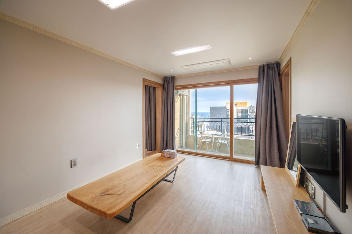 A room with a wooden table, a TV, and a balcony with a view of buildings.
